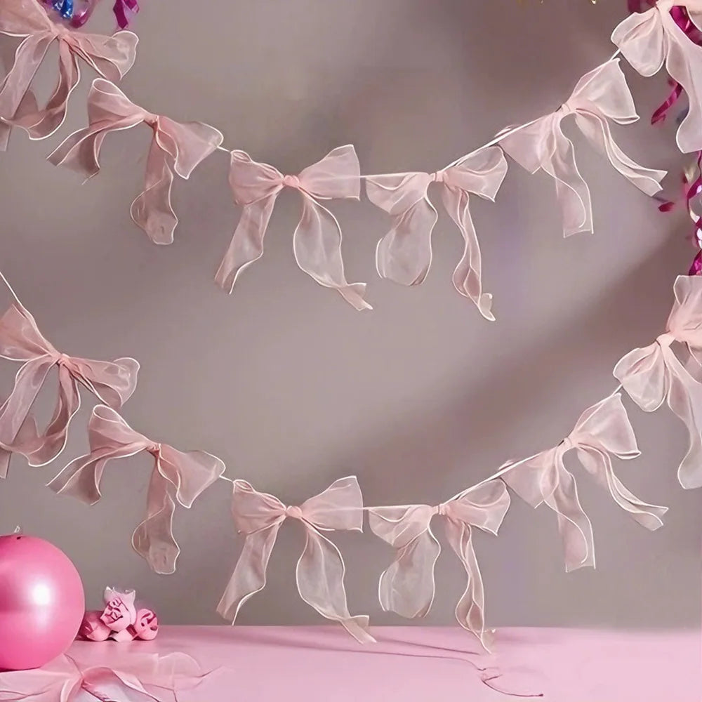 A delicate pink sheer ribbon bow knot banner garland is displayed against a light background.