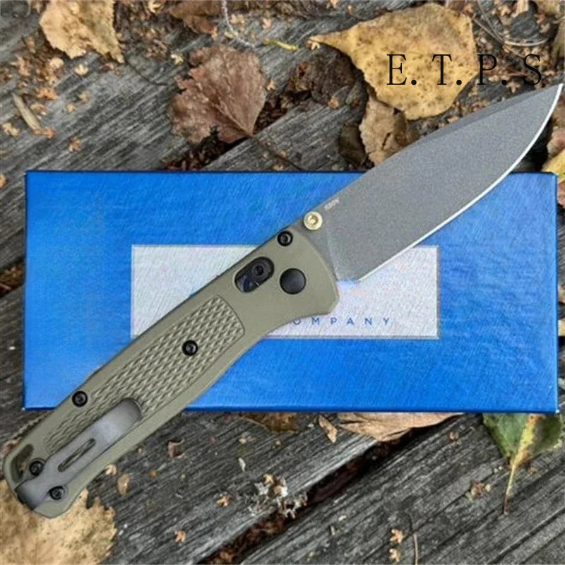 A CPM-20CV folding pocket knife with a drop point blade resting on a blue box amidst dry leaves.