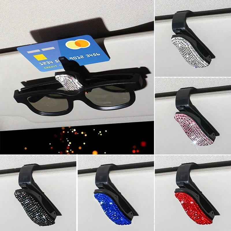 Black sunglasses clip with crystal rhinestones and colored accents mounted on a car visor.