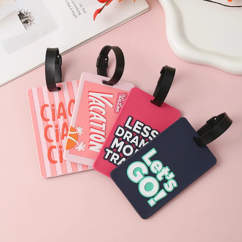 Pink and dark blue silicone luggage tags with letter designs and black straps on a pink background.