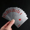 A hand holds a fan of 24K gold waterproof playing cards showing the numbered and face cards.