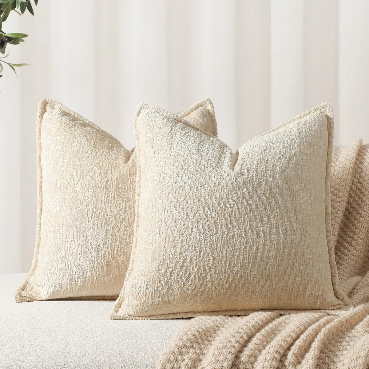 A close-up of a cream chenille throw pillow cover resting on a light-colored surface.