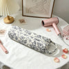 A pink quilted cotton hair dryer storage bag with a handle is displayed on a white table next to a pink hair dryer.