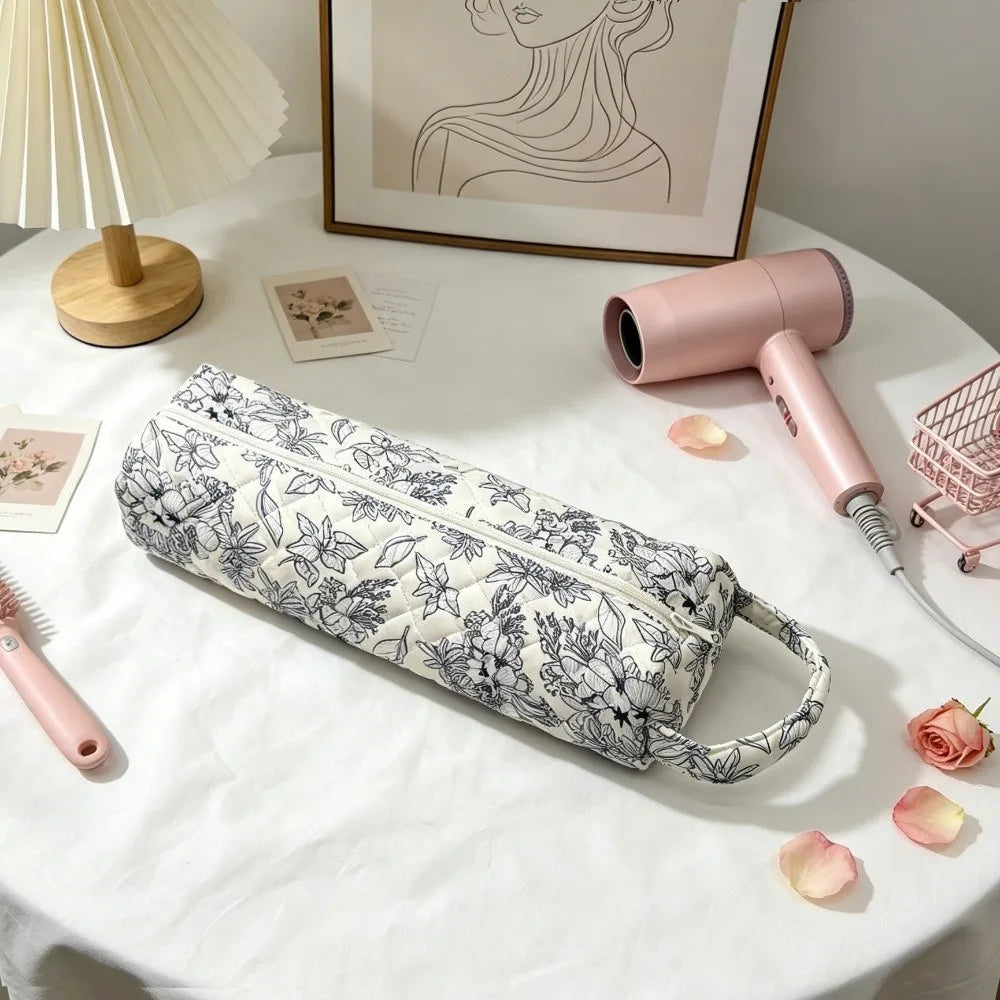 A pink quilted cotton hair dryer storage bag with a handle is displayed on a white table next to a pink hair dryer.