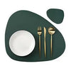 A set of gold-colored cutlery and a white plate are displayed on a dark green placemat.