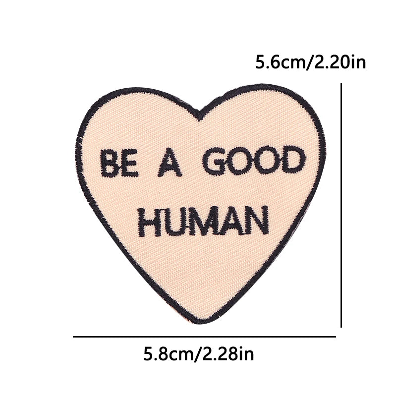 A light pink heart shaped patch embroidered with the text BE A GOOD HUMAN