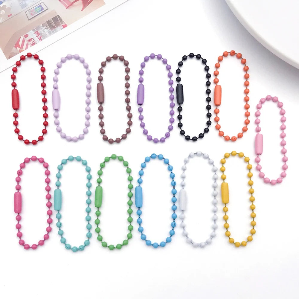 A collection of 20 colorful ball bead chains in various colors and lengths laid out on a white surface.