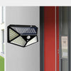 A black solar powered motion sensor wall light with 100 LEDs mounted on a white wall next to a red door frame.