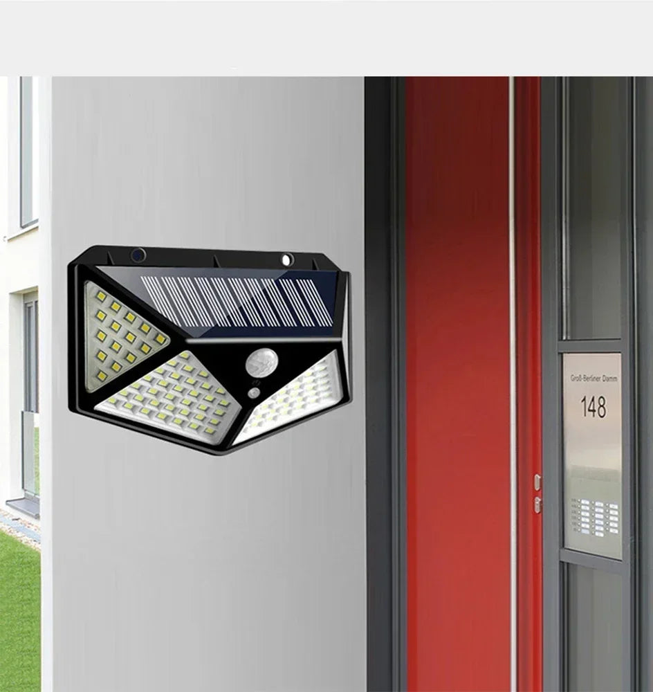 A black solar powered motion sensor wall light with 100 LEDs mounted on a white wall next to a red door frame.