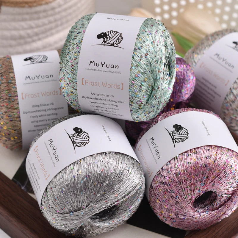 Three spools of glitter yarn in various shades including silver, pink, and green with labels