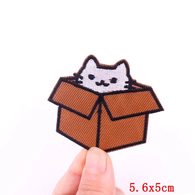 A brown embroidery patch shaped like a cat sitting inside a cardboard box.