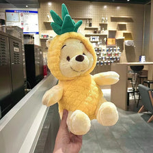 A hand is holding a yellow Winnie the Pooh plush toy with green foliage on its head.