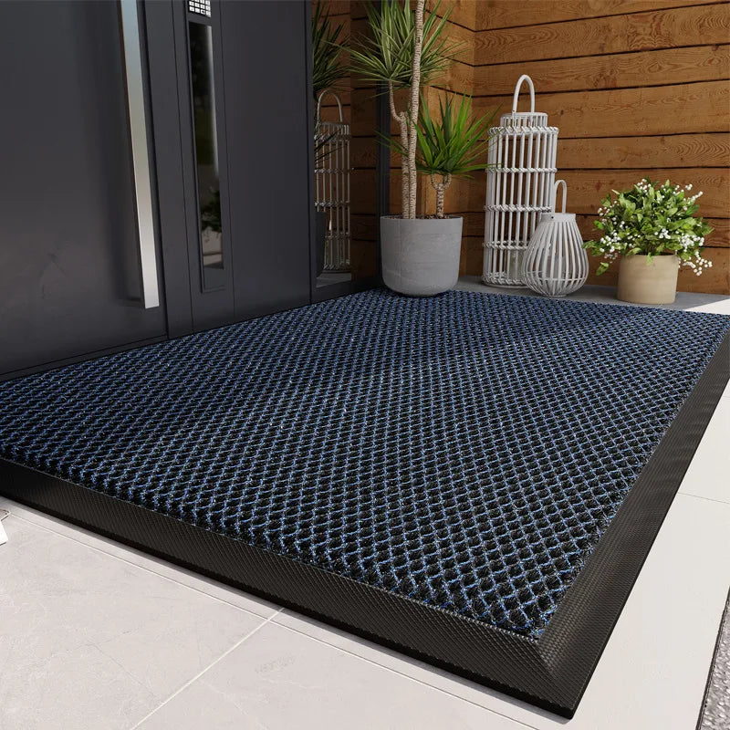 A dark blue non-slip doormat with a diamond pattern placed on a light gray floor near a wooden wall.