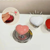 A heart-shaped toilet flush button in pink and white is shown on a white surface.