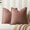 A close-up of two textured, dusty rose chenille throw pillows resting on a beige knitted blanket.
