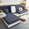 A modern gray sofa with a white slipcover featuring a rectangular back panel and decorative floral cushions.