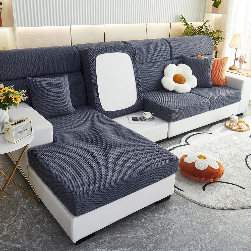 A modern gray sofa with a white slipcover featuring a rectangular back panel and decorative floral cushions.