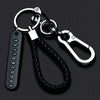 A silver keychain featuring a personalized phone number engraved on a tag and attached to a braided black leather rope.