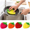 A hand is using a yellow strawberry scrubber sponge in a stainless steel sink for cleaning dishes.