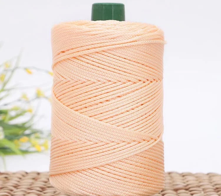 A spool of light peach colored crochet ice rope with a green cap, resting on a woven mat.