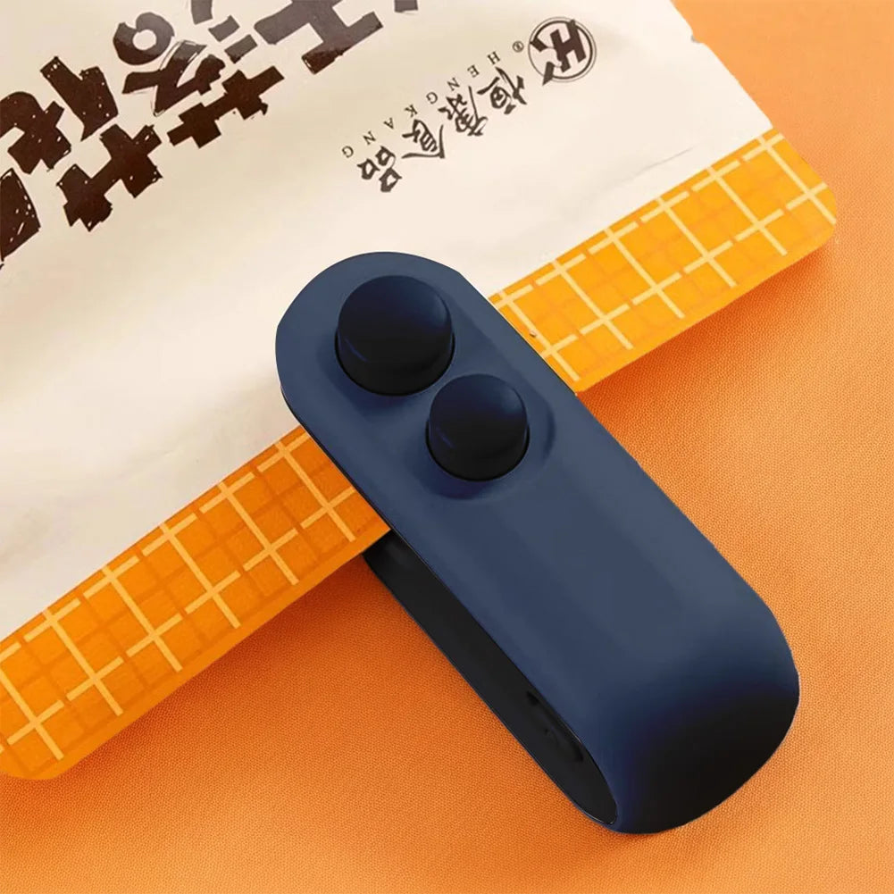 A dark blue portable 2-in-1 bag sealer and cutter rests on an orange surface next to a piece of white paper.