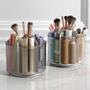 A clear rotating makeup brush holder with six compartments filled with various makeup brushes and tools.