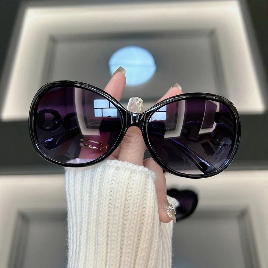 A hand holds a pair of purple square vintage sunglasses against a bright background.