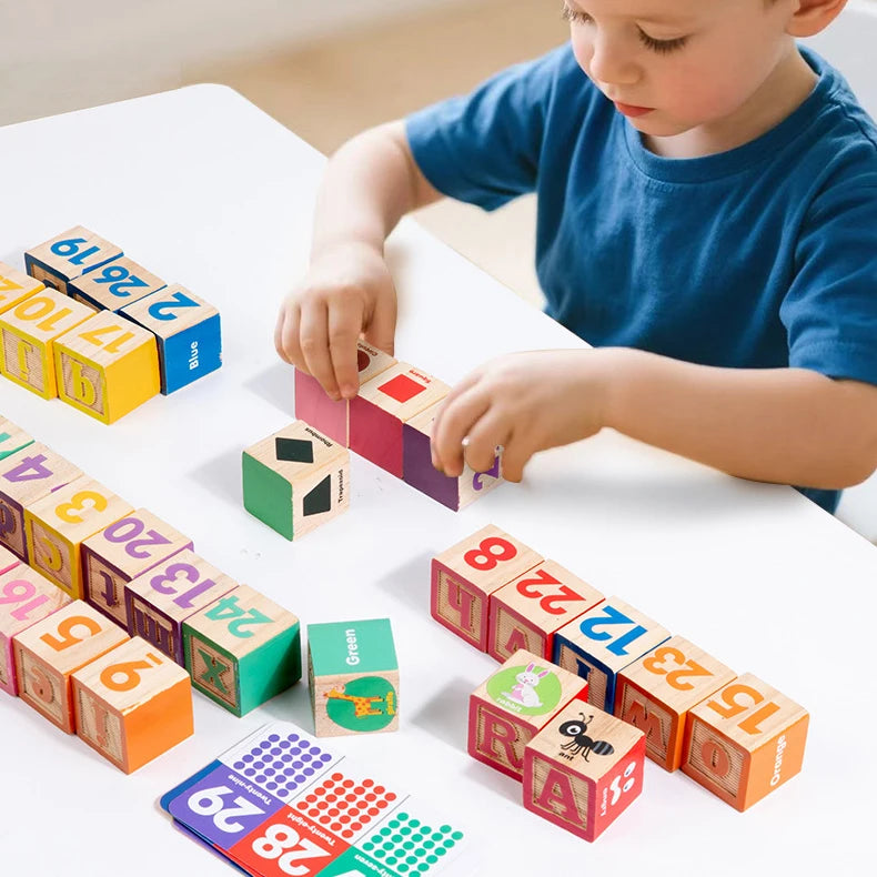 A young child is building with colorful wooden blocks and letter tiles on a white table.