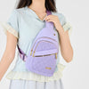 A woman holds a purple quilted crossbody sling bag against a light blue shirt.
