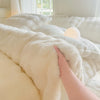 A hand is touching a fluffy white fleece duvet cover with a rabbit design on a bed.