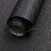 Roll of black embossed silk self-adhesive wallpaper being unrolled