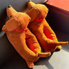 A pair of brown plush cartoon dog slippers with red accents resting in a dark box.