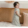 A smiling baby wearing a light green breathable cotton sleep sack in a natural indoor setting.