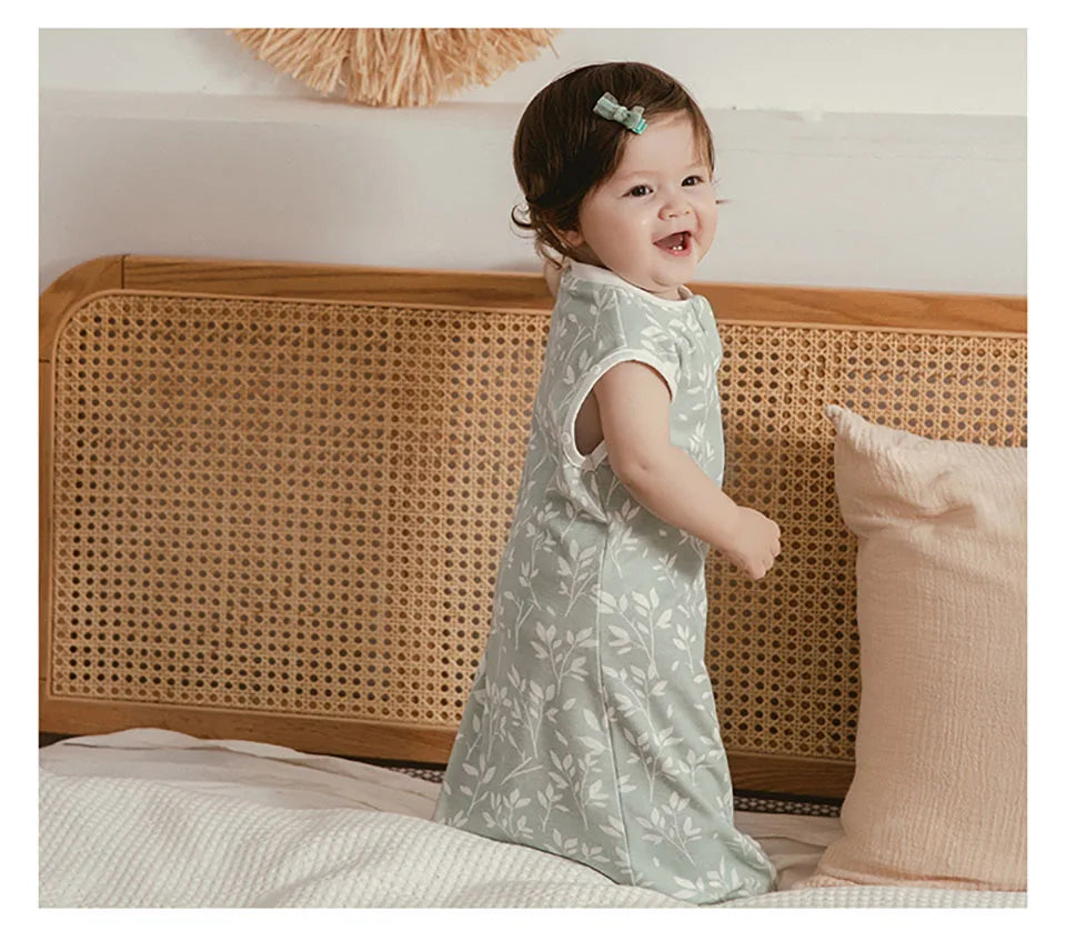 A smiling baby wearing a light green breathable cotton sleep sack in a natural indoor setting.