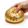 A hand is squeezing a golden, squishy dumpling-shaped fidget toy with cute facial features.