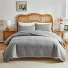 A gray quilted queen bedspread set with matching pillow shams displayed on a wooden bed frame.