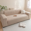 A beige plush sofa cover with a light-colored rug and decorative pillows in a bright room.