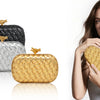 A woman holds a gold woven clutch bag and a silver woven clutch bag against a white background.