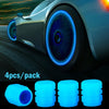 Pack of four luminous blue glow-in-the-dark tire valve caps shown next to a modern car wheel.