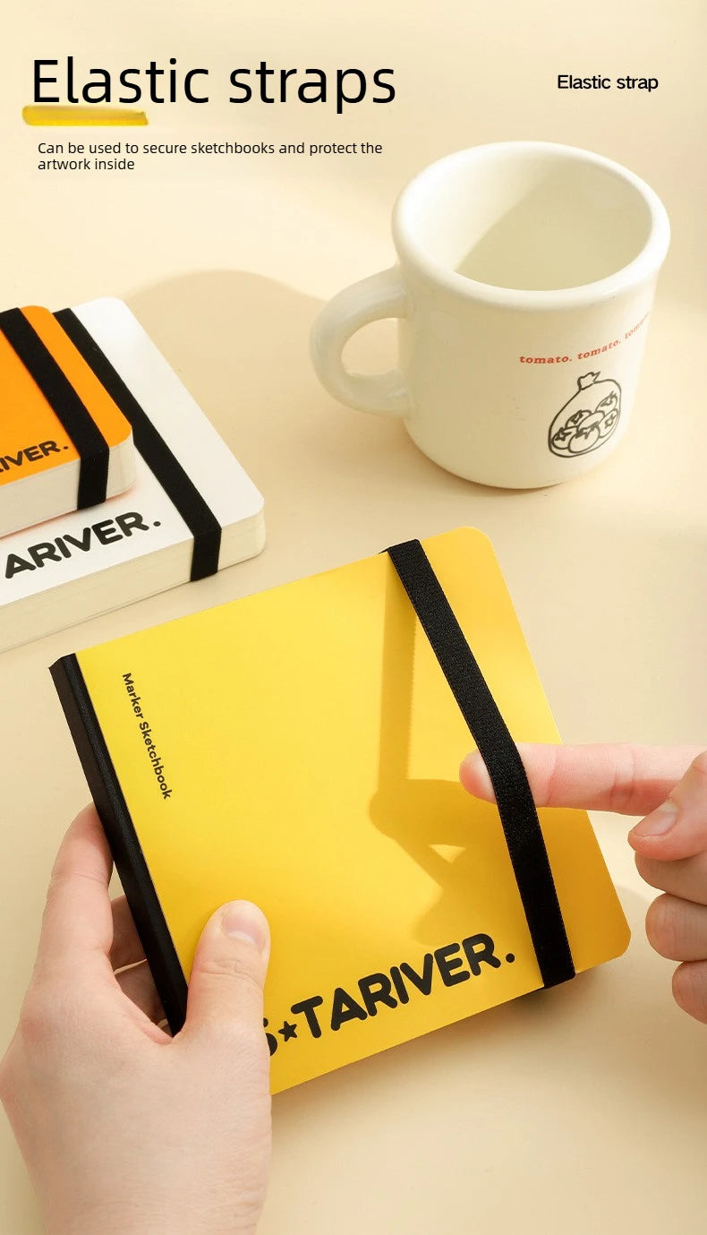 A yellow sketchbook is secured with a black elastic strap, shown next to a white mug.
