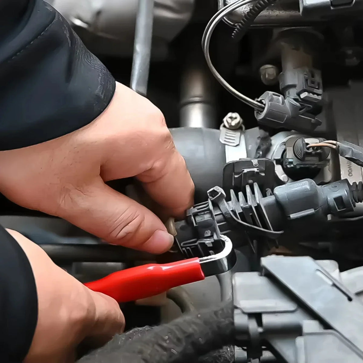 Eine Hand benutzt ein rotes Werkzeug, um einen elektrischen Steckverbinder an einem Fahrzeugbauteil zu trennen.