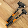A black octagonal bush hammer with an orange anti-slip handle resting on a wooden surface.