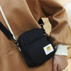 A black mini canvas crossbody bag is worn on a brown jacket, featuring a leather strap and hardware.