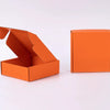 Eine offene orangefarbene Wellpappkarton und eine geschlossene orangefarbene Verpackung auf einer weißen Oberfläche.