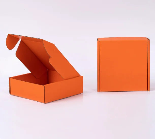 Eine offene orangefarbene Wellpappkarton und eine geschlossene orangefarbene Verpackung auf einer weißen Oberfläche.