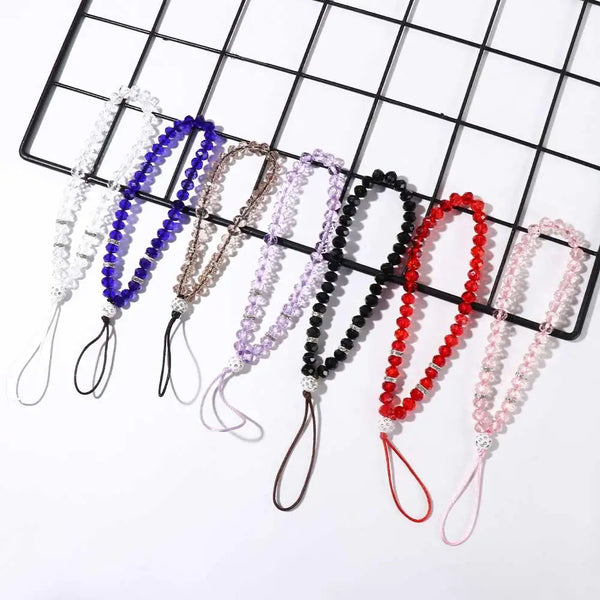 A collection of crystal bead phone lanyards with wrist straps arranged on a black grid.