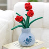 A vase holding three red artificial roses with green stems, set against a white towel and a book.