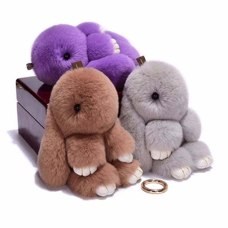 A set of fluffy angel bunny keychains in purple and gray with pom pom tails