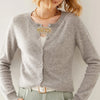 A light gray knit sweater with a gold decorative clip on the collar, worn by a person.
