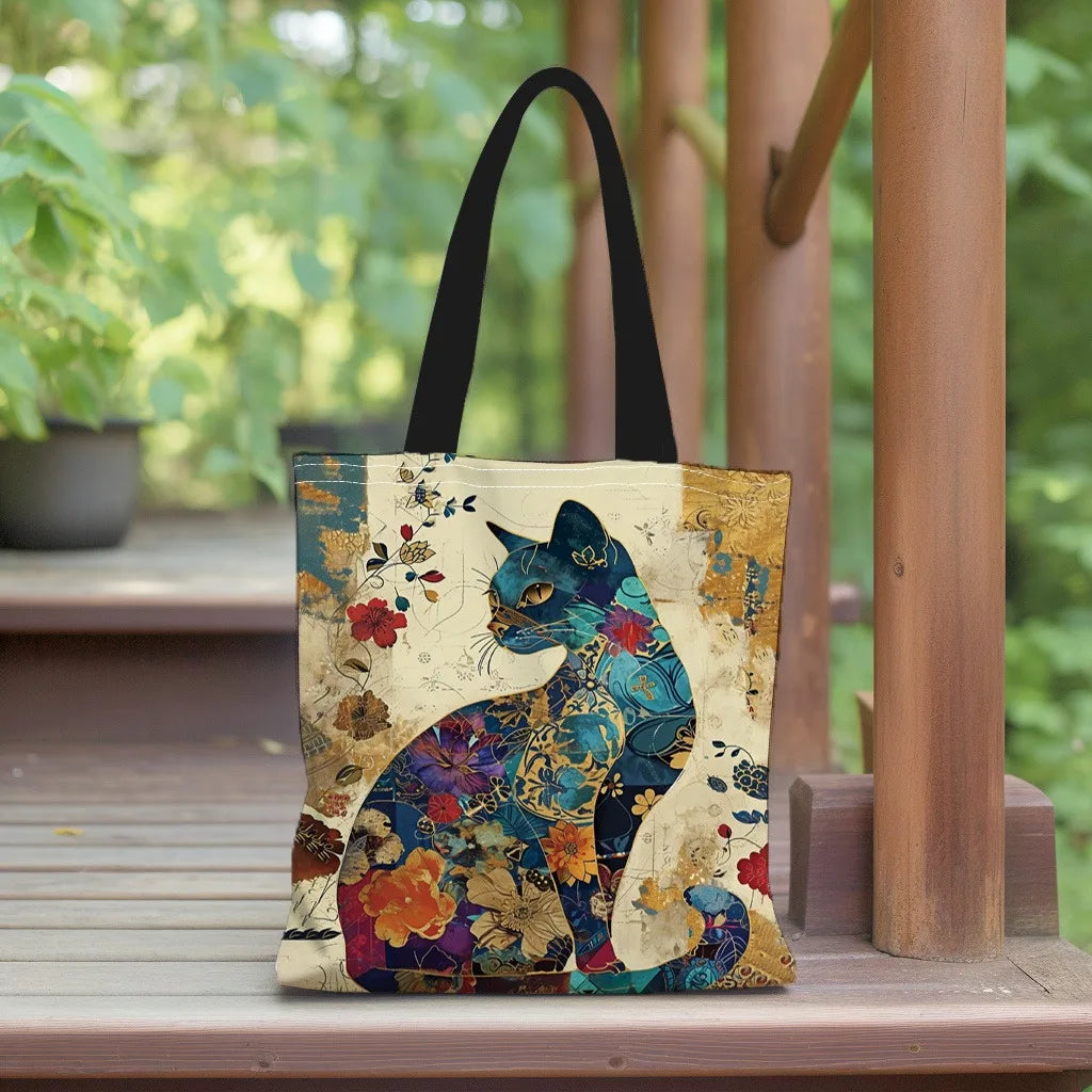 A canvas tote bag featuring a watercolor illustration of a blue and teal cat amidst floral patterns, displayed on a wooden su
